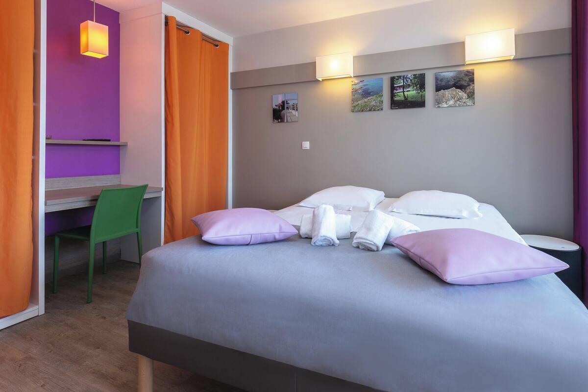 Una habitación de hotel con cama, escritorio, silla y mesita de noche.