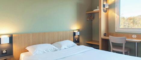 A hotel room with a bed, bedside lamps, a desk with a chair, and a window.