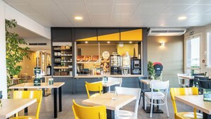 A modern cafe with yellow and white chairs, a counter with a coffee machine, and a visible menu board. - B&B HOTEL Brive-la-Gaillarde (Ussac)