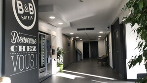 A hotel lobby with a reception desk, a staircase, and a large plant. - B&B HOTEL Brive-la-Gaillarde (Ussac)