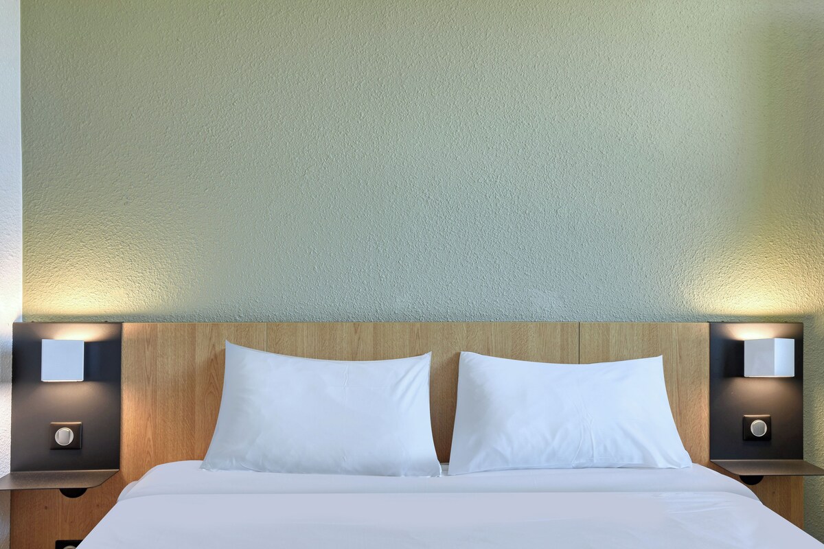 A hotel room with a wooden headboard, two white pillows, and two bedside lamps.