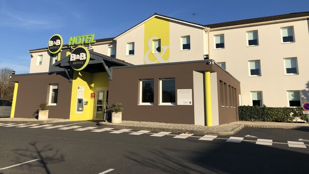 A B&B hotel with a yellow and brown facade, a signboard, and a parking area with marked spaces. - B&B HOTEL Brive-la-Gaillarde (Ussac)