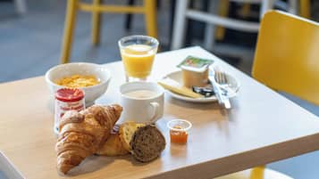 Una mesa de desayuno con cruasanes, una taza de café, un vaso de jugo de naranja, un frasco pequeño de mermelada y un plato con un pastel.