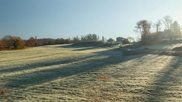 A rural landscape with a clear sky, a frost-covered field, and a few buildings in the distance.