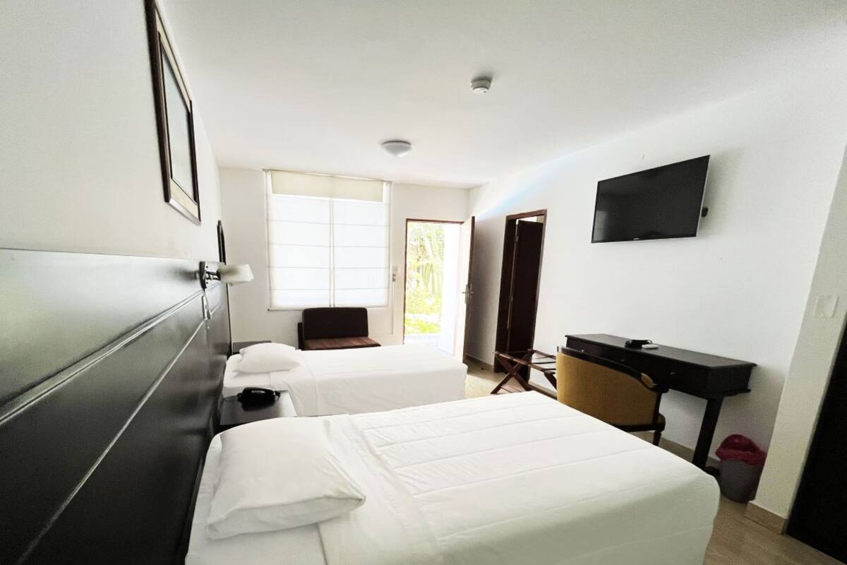 A hotel room with two beds, a desk, a chair, a TV, and a window.