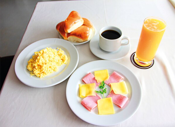 A breakfast table with scrambled eggs, ham and cheese, a croissant, a cup of coffee, and a glass of orange juice.
