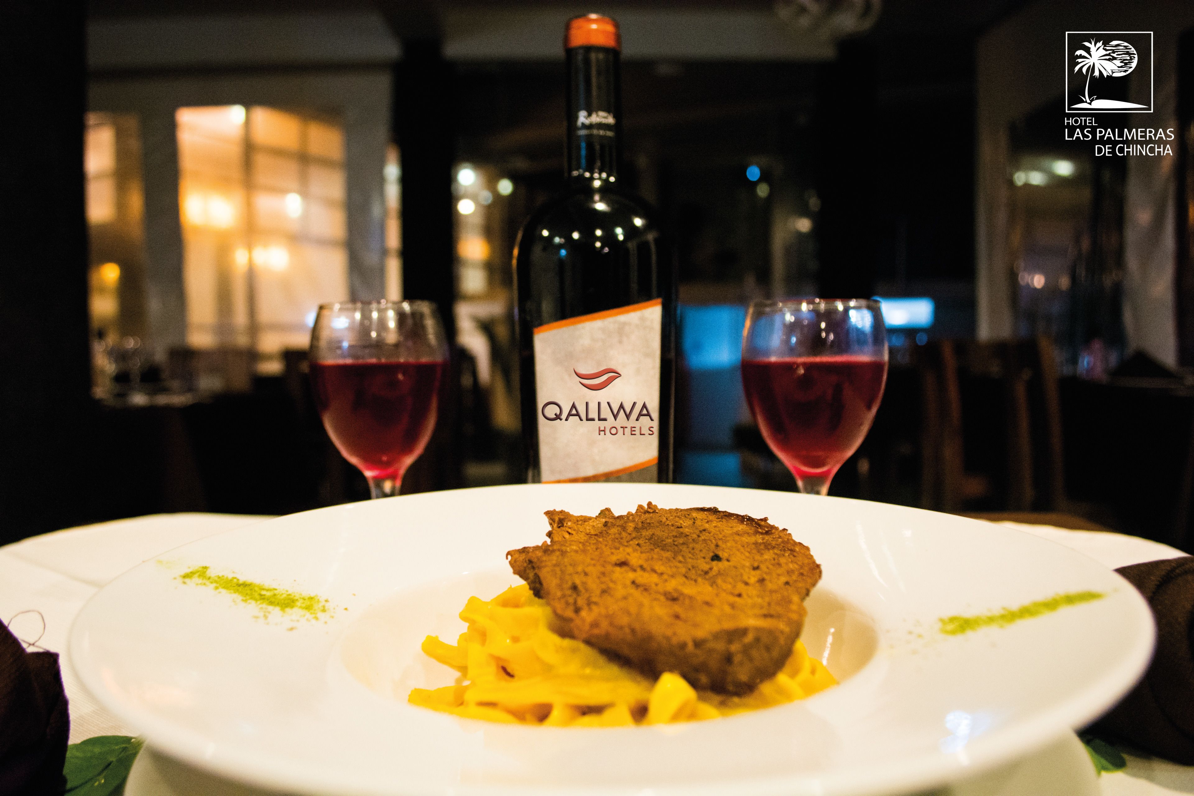 A plate of food with a bottle of Qallwa Hotels wine and two glasses of red wine.