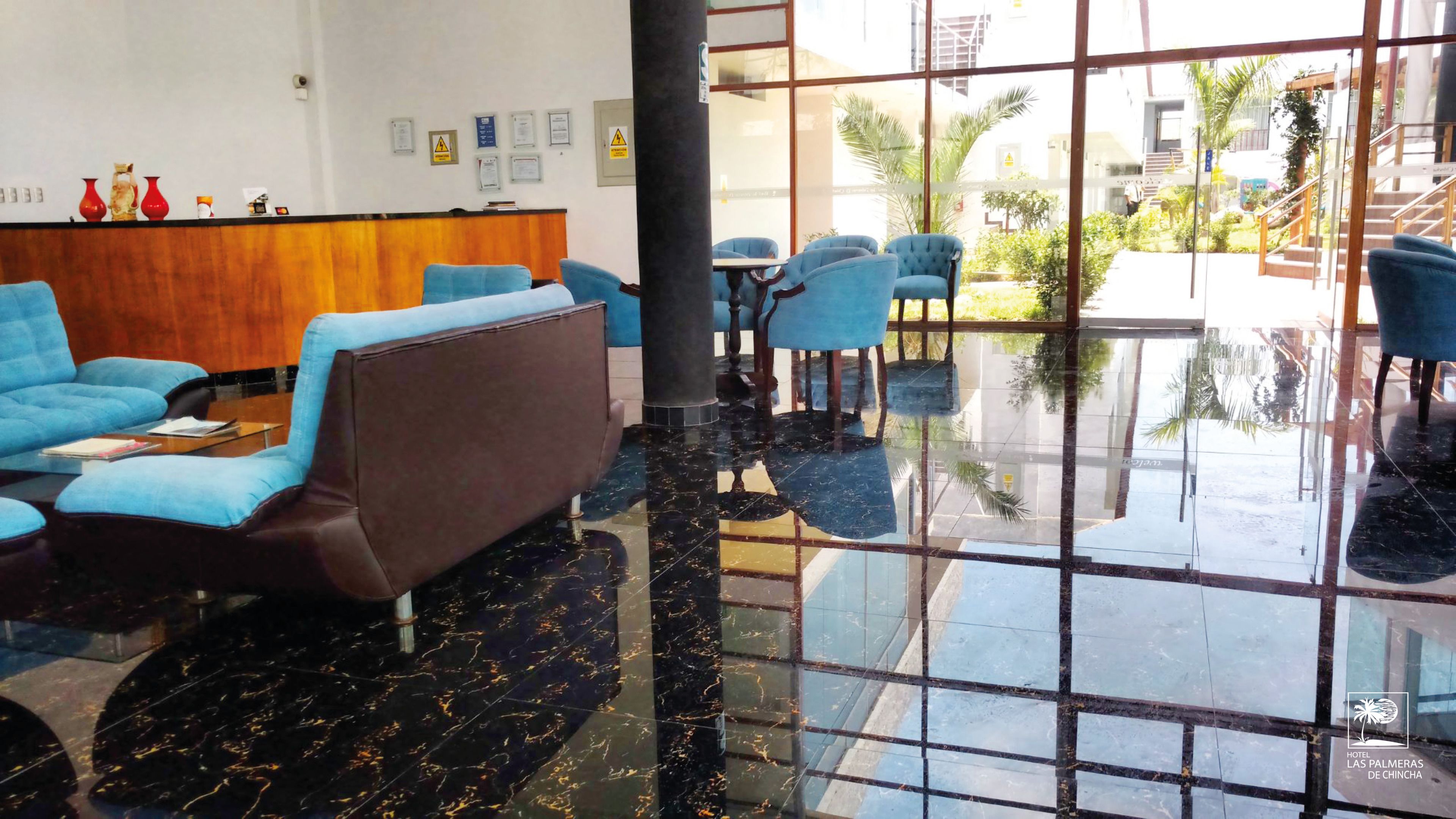 Een hotellobby met blauwe banken, een receptiebalie en een glazen vloer die het buitengebied weerspiegelt.