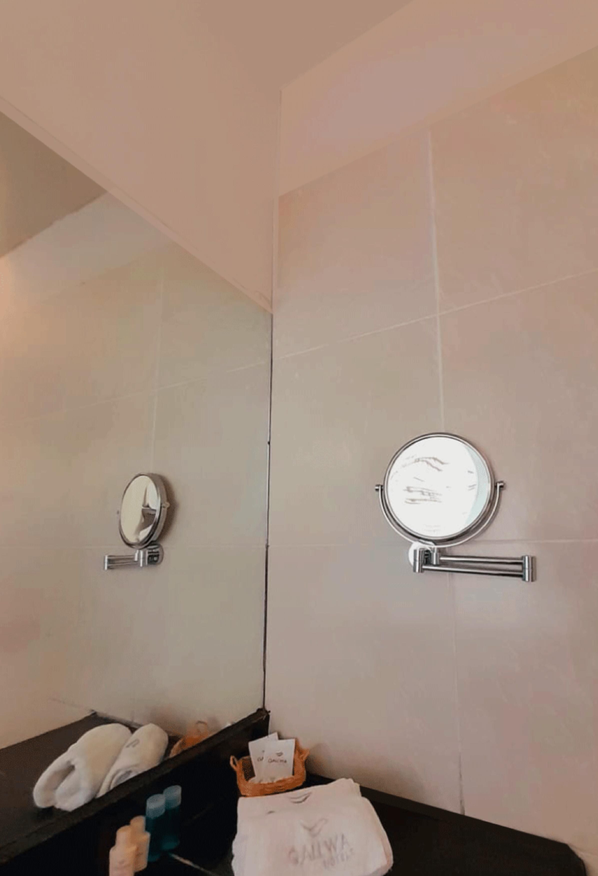Um banheiro com dois espelhos fixados na parede, porta-toalhas e um prateleira com artigos de higiene pessoal.