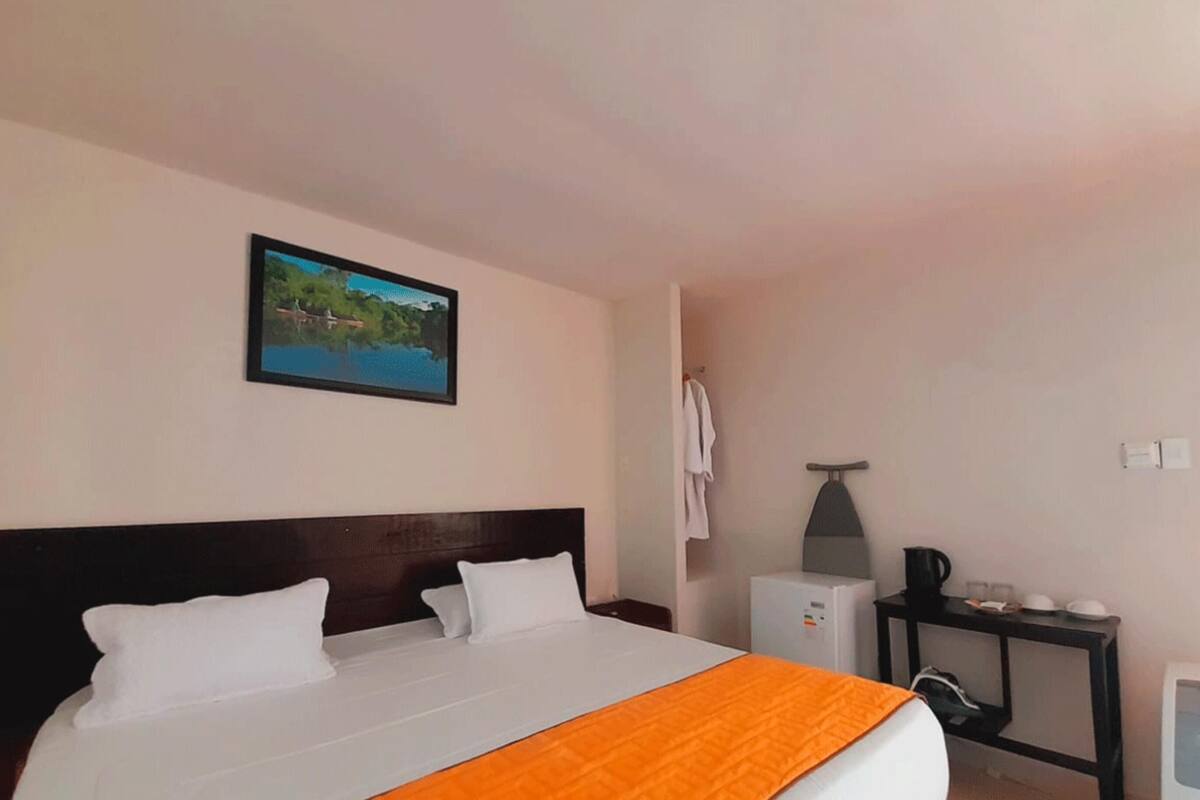 A hotel room with a bed, a nightstand, a table with a lamp, a picture on the wall, and a window.