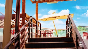 Un escalier en bois mène à un espace extérieur aménagé avec des chaises rouges et un parasol jaune.