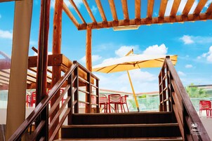 Una escalera de madera que conduce a un área de estar al aire libre con sillas rojas y un paraguas amarillo.