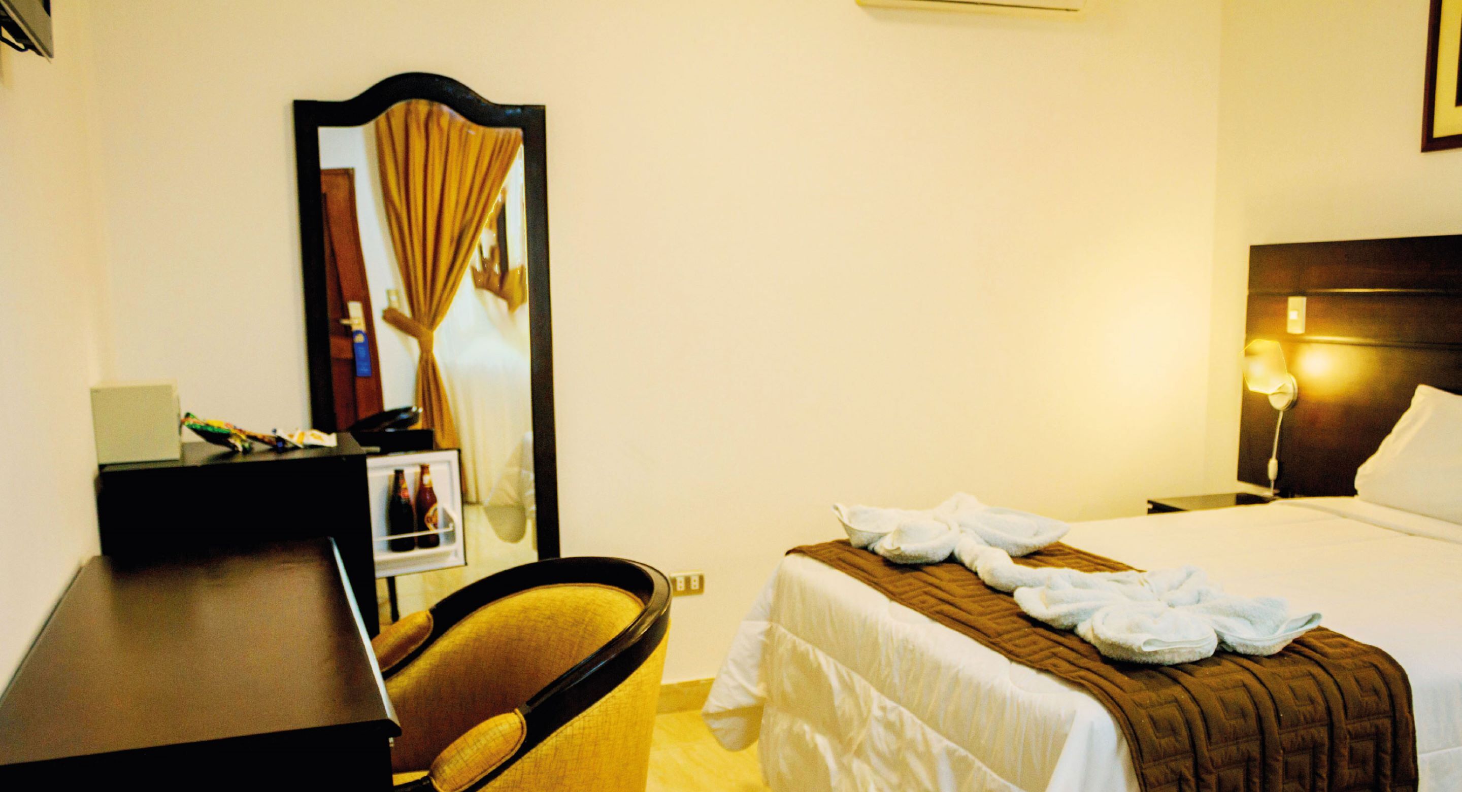 Une chambre d’hôtel comprenant un lit, un bureau, une chaise, un miroir et une table de chevet.