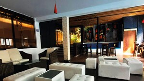 Un vaste espace salon avec des canapés et des poufs blancs, un coin bar avec des tabourets, et un escalier menant à un niveau supérieur.