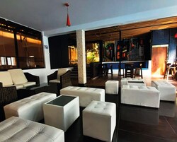 Un amplio salón con sofás y otomanes blancos, una zona de bar con taburetes y una escalera que conduce a un nivel superior.