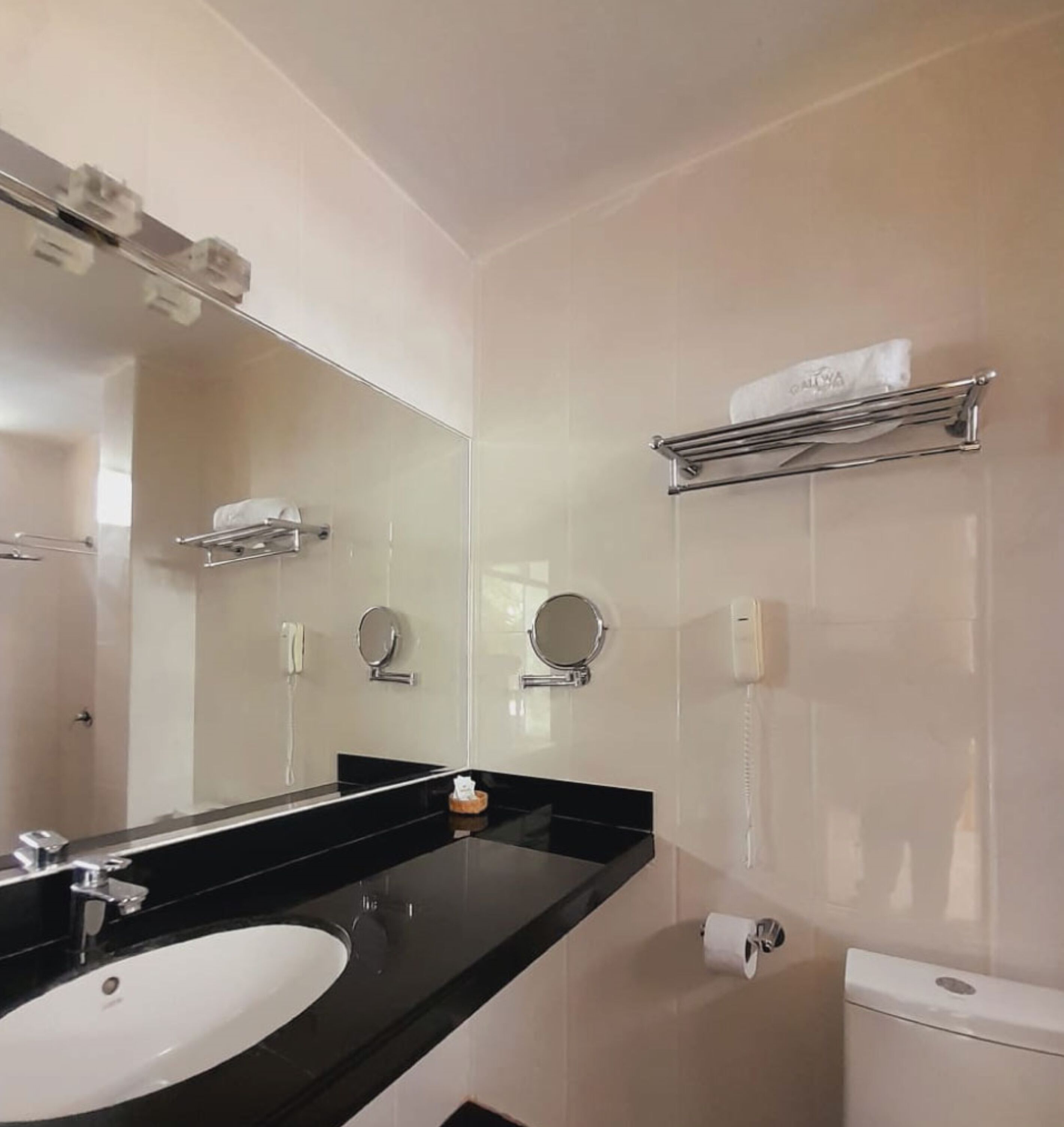 A modern bathroom with a black countertop, a white sink, a mirror, a towel rack, and a toilet.