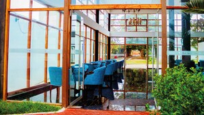 L’intérieur moderne d’un hôtel présente un espace de restauration avec des chaises bleues et une vue sur un jardin, grâce à de grandes fenêtres.