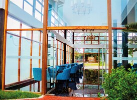 Un interior de hotel moderno con un comedor que tiene sillas azules y vistas a un jardín a través de amplios ventanales.