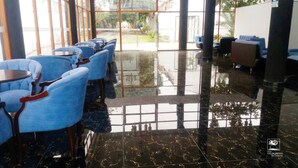 Un hall d’hôtel avec des fauteuils et des tables recouverts d’un tissu bleu, un sol en marbre noir poli et de grandes fenêtres donnant sur l’extérieur.