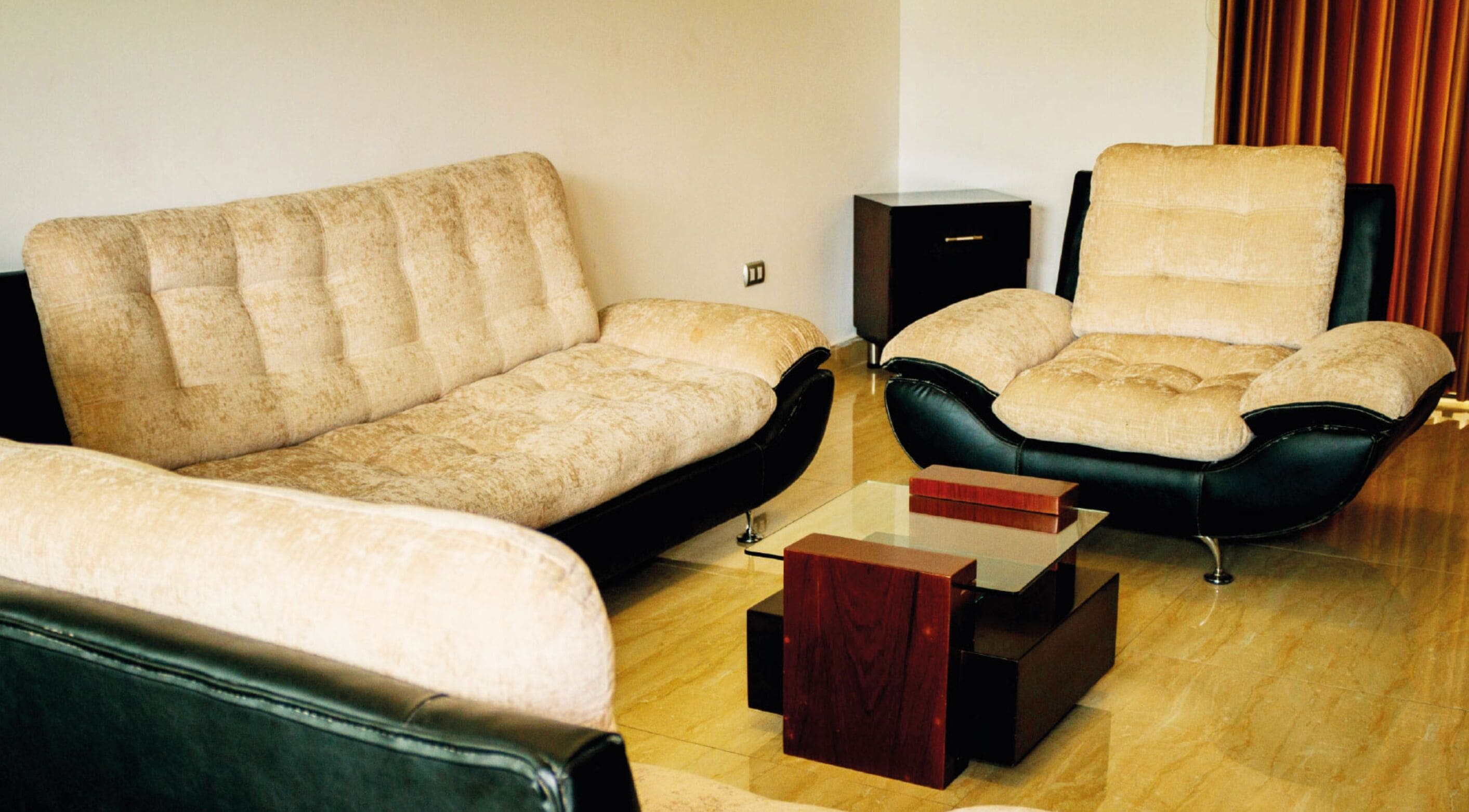 A living room with a beige sofa, a black leather armchair, and a wooden coffee table.