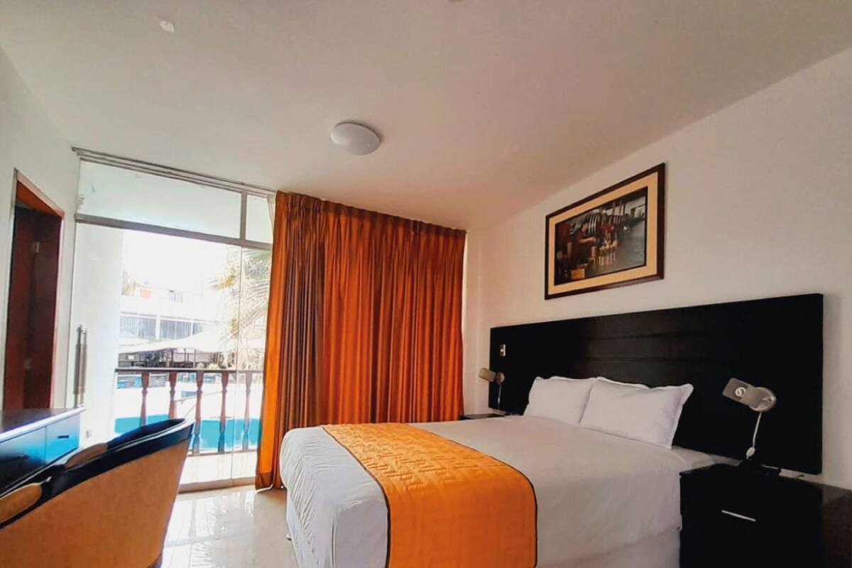 A hotel room with a large bed, a nightstand, a desk, and a window with curtains.
