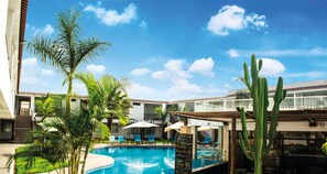 A pool area with palm trees, a cactus, and a building with a balcony. - Qallwa Chincha (Sunampe)