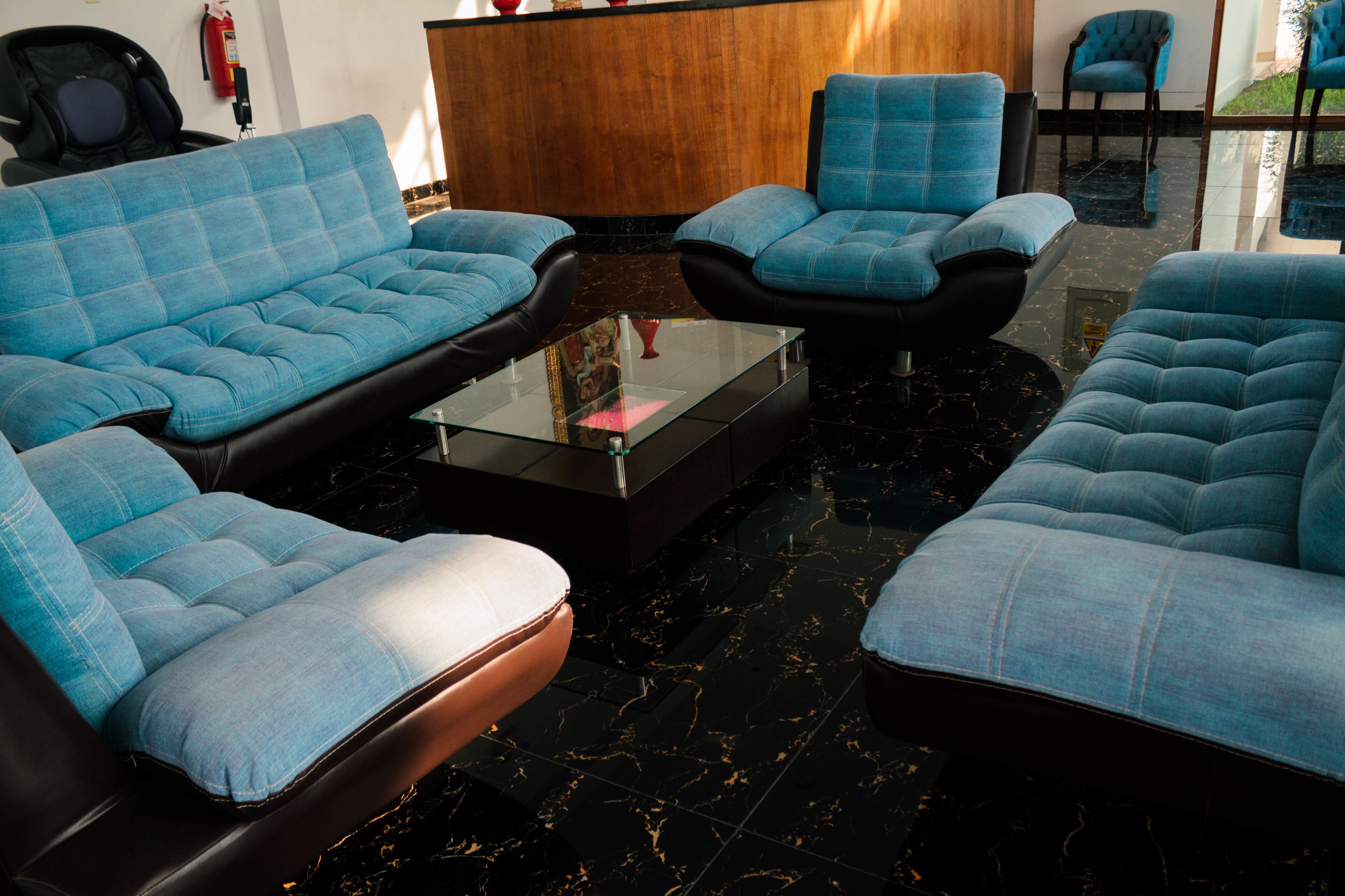 A modern lobby with blue upholstered sofas and armchairs, a glass coffee table, and a wooden reception desk.