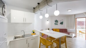 A modern kitchen with white cabinets, a stainless steel sink, and a dining area with a white table and yellow chairs. - Apartamentos Datasol (San Bartolomé de Tirajana)