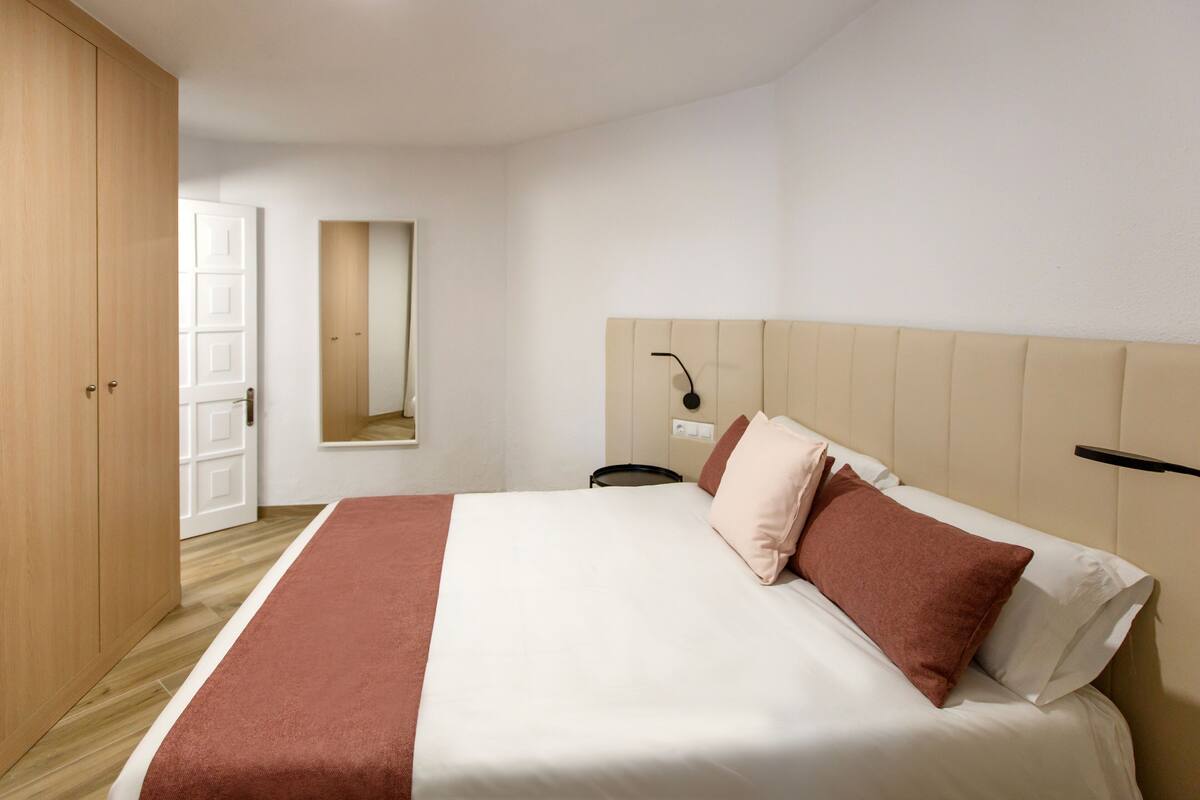 A neatly arranged bedroom with a bed, a bedside table, a mirror, and a wardrobe.