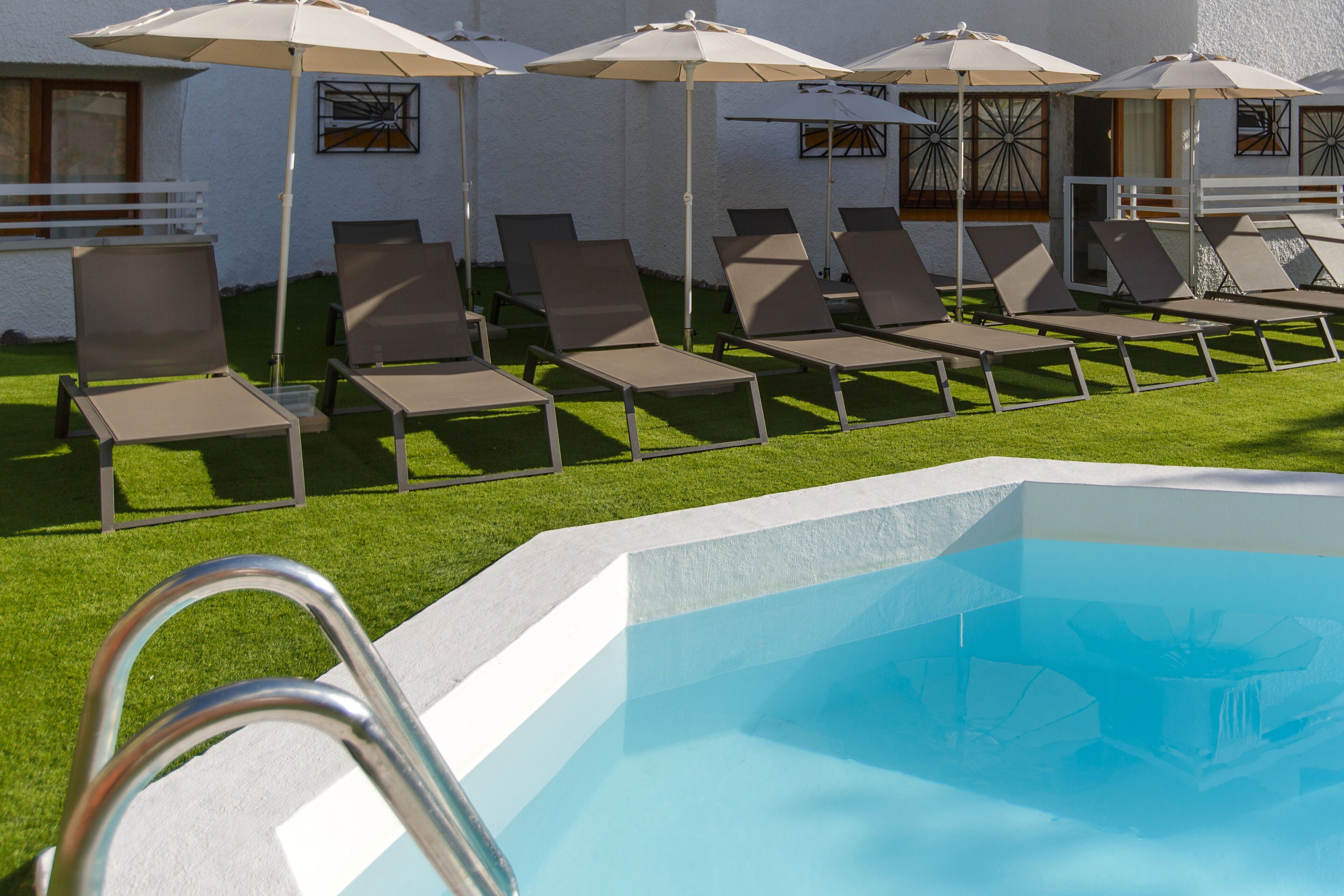 A pool area with lounge chairs and umbrellas, a clear pool, and a white building with windows.
