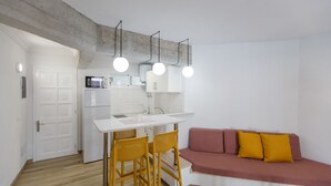 A compact kitchen with a white countertop, a microwave, and hanging lights. There is a wooden dining table with chairs and a red sofa with yellow cushions. - Apartamentos Datasol (San Bartolomé de Tirajana)