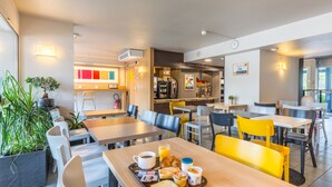 Un espace repas moderne avec des tables et des chaises, une machine à café et une plante.