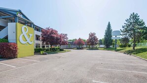 Un parking avec un bâtiment sur lequel est affiché un grand panneau en forme de « & ».