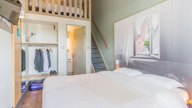 Une chambre d’hôtel comprenant un lit, une armoire, un miroir, une télévision et un escalier menant à une couchette supérieure.
