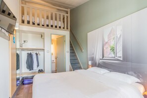 Habitación de hotel con una cama, armario, espejo, televisión y una escalera que lleva a una litera superior.