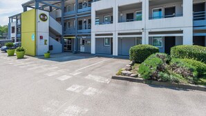 Un hôtel à plusieurs étages, doté d’un design moderne, comprenant un parking et un petit jardin agrémenté de plantes en pot.