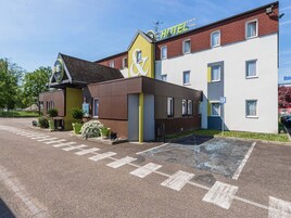 Un hotel con una fachada distintiva de color amarillo y marrón, un cartel que indica que es un hotel, y un estacionamiento con espacios delimitados.