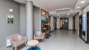 A modern hotel lobby with a reception desk, seating area, and a large pillar. - B&B HOTEL Strasbourg Sud Ostwald (Ostwald)