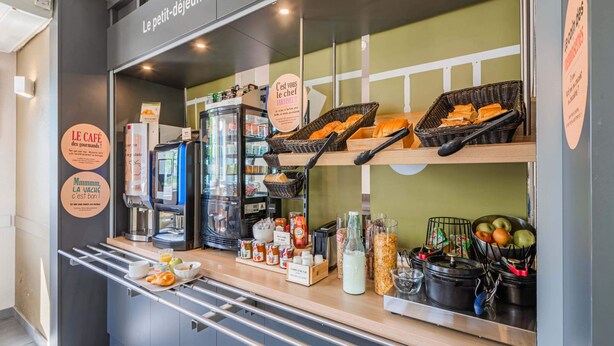 A café counter with a coffee machine, baskets of bread, and a fruit bowl. - B&B HOTEL Strasbourg Sud Ostwald (Ostwald)