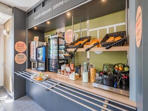 Una barra de café con una máquina de café, cestas de pan y un bol de fruta.