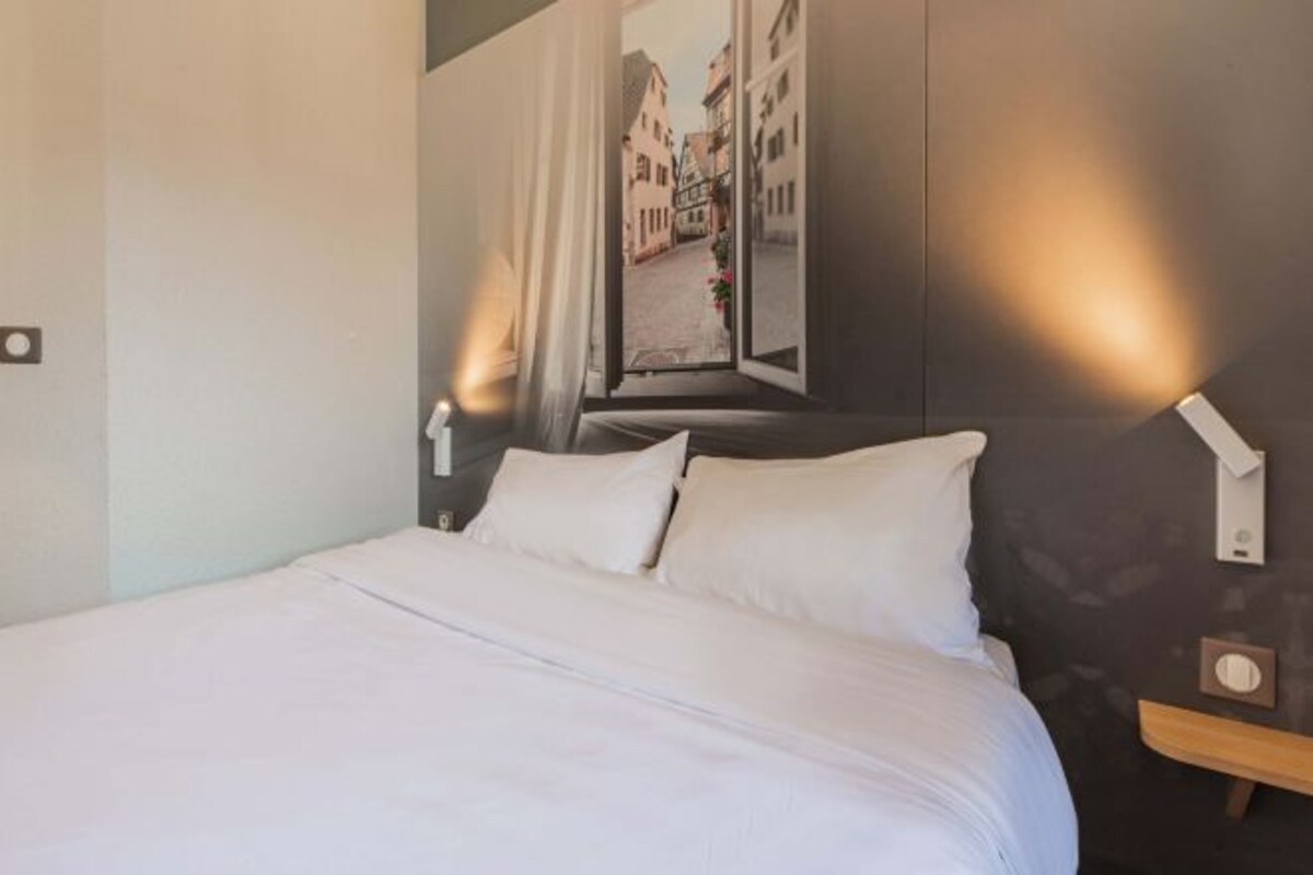 A neatly made bed with white linens in a hotel room.