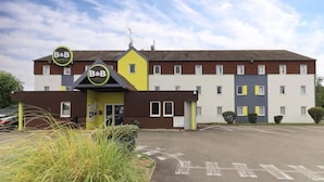 A B&B hotel with a modern design, featuring a yellow and brown facade, multiple windows, and a parking lot. - B&B HOTEL Beaune Sud (2) (Beaune)