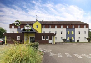 Un hotel B&B con diseño moderno, que presenta una fachada amarilla y marrón, múltiples ventanas y un estacionamiento.