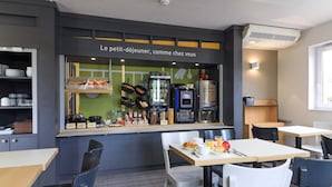 A café with a counter displaying breakfast items, a coffee machine, and a menu board. There are tables and chairs for seating. - B&B HOTEL Beaune Sud (2) (Beaune)