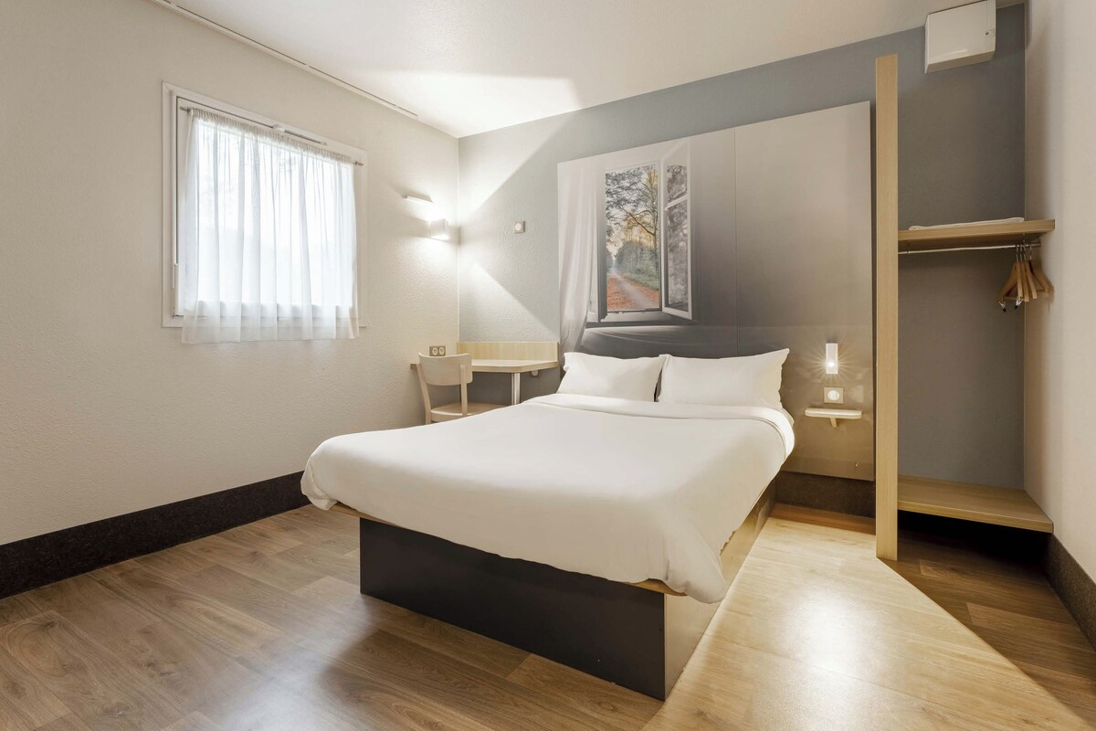 A bedroom with a bed, a window with curtains, a bedside table, and a wall-mounted light.