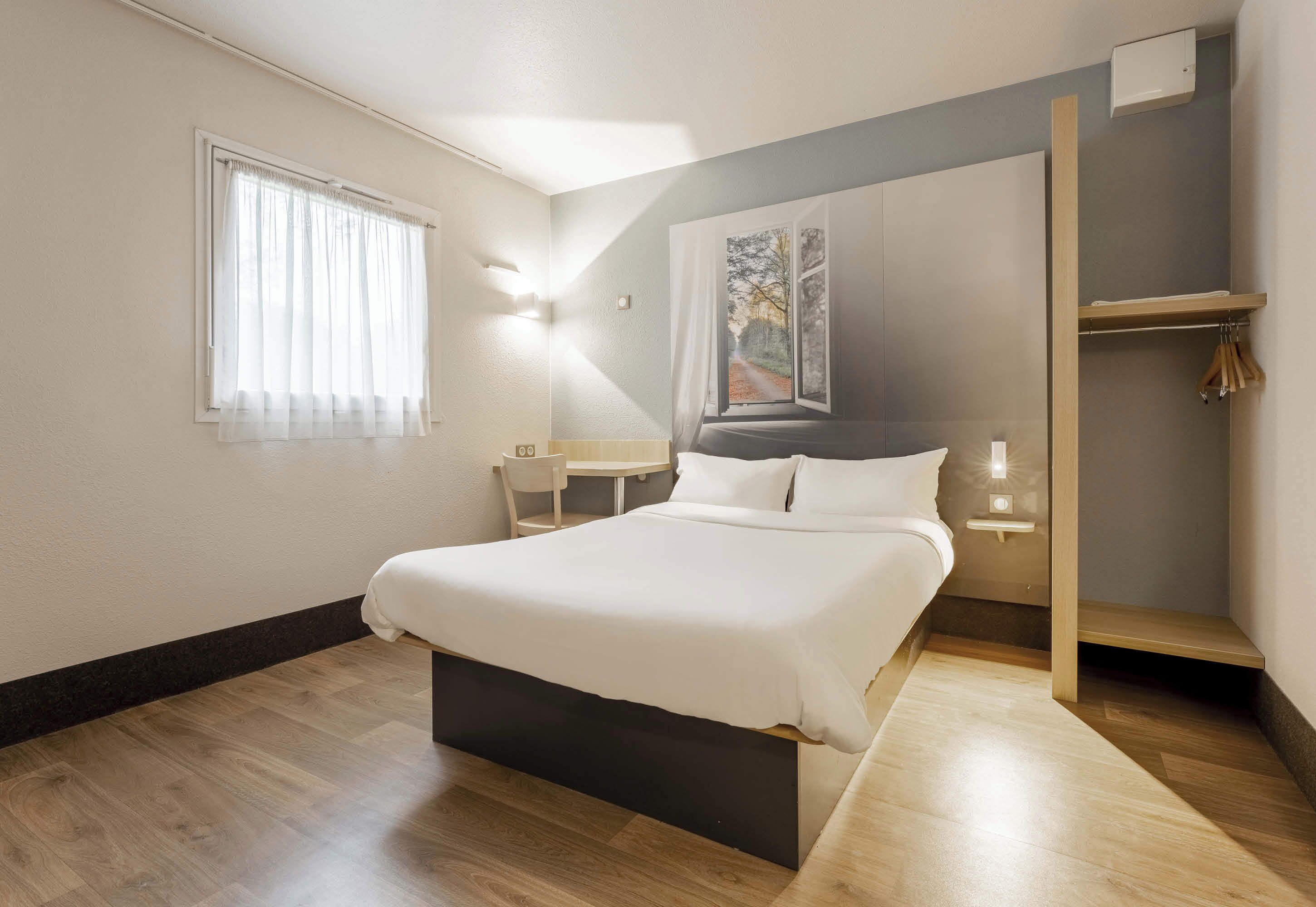 Een slaapkamer met een bed, nachtkastjes, een raam met gordijnen, een wandlamp en een schilderij.