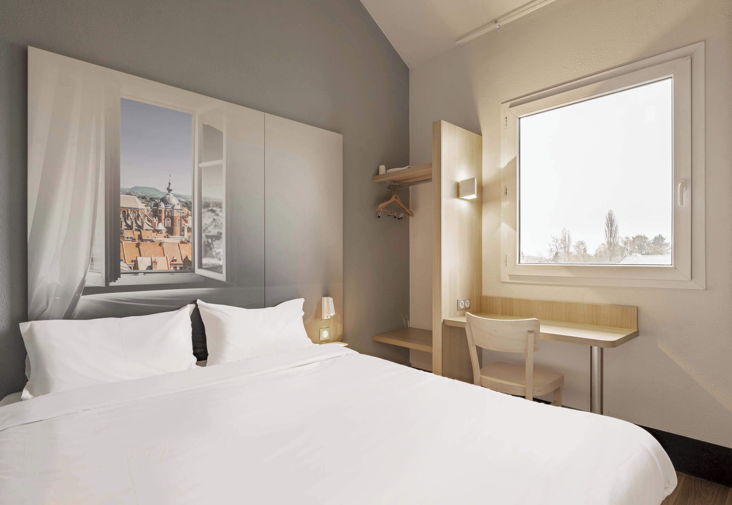 Een hotelkamer met een bed, een bureau, een stoel, een raam met uitzicht en een kledingkast.