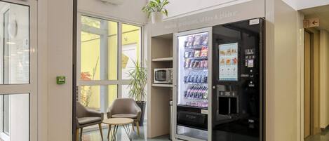 A modern lobby with a vending machine, seating area, and a potted plant.