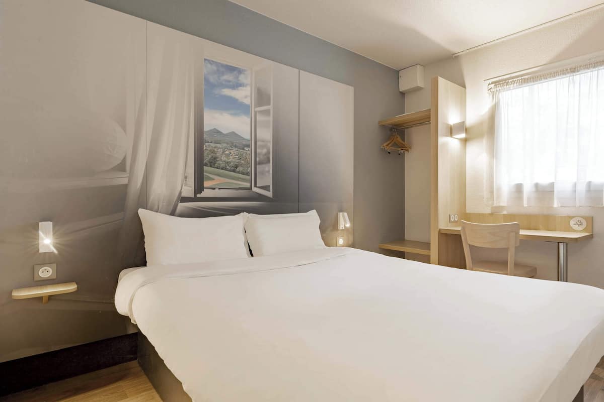 A hotel room with a large bed, a desk, and a chair.