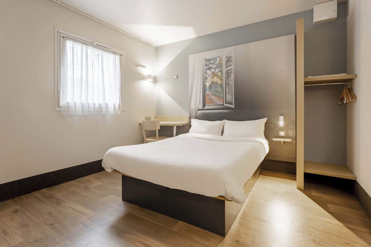 A bedroom with a bed, a window with curtains, a bedside table, and a wall-mounted light.